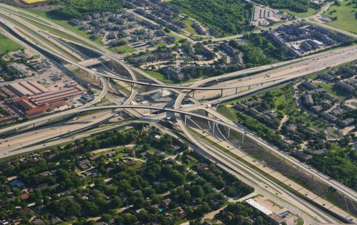 intersecting highways coming from four different directions, creating a cross, surrounded by greenery, buildings, and cars.