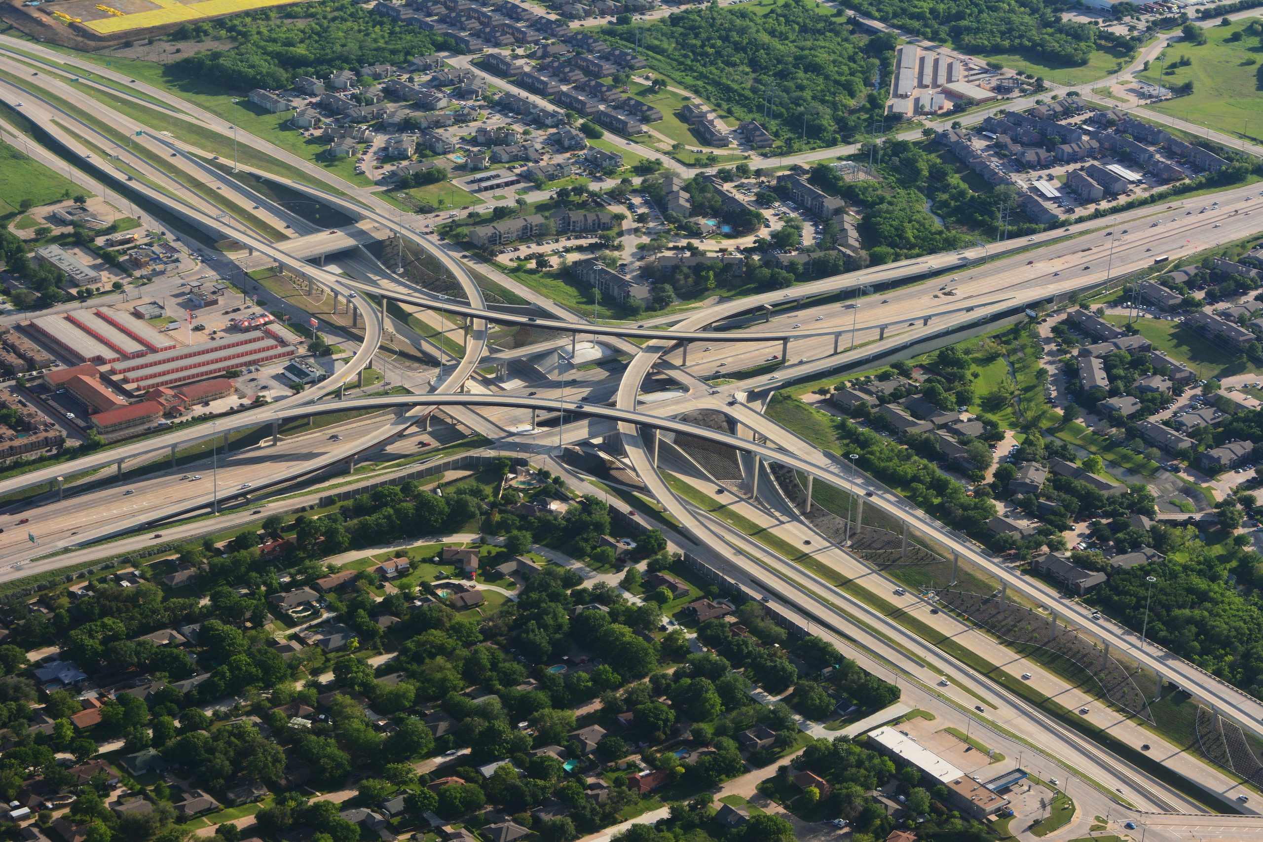 irina-blok-QwmB-VgL7vs-unsplash intersecting highways coming from four different directions, creating a cross, surrounded by greenery, buildings, and cars.